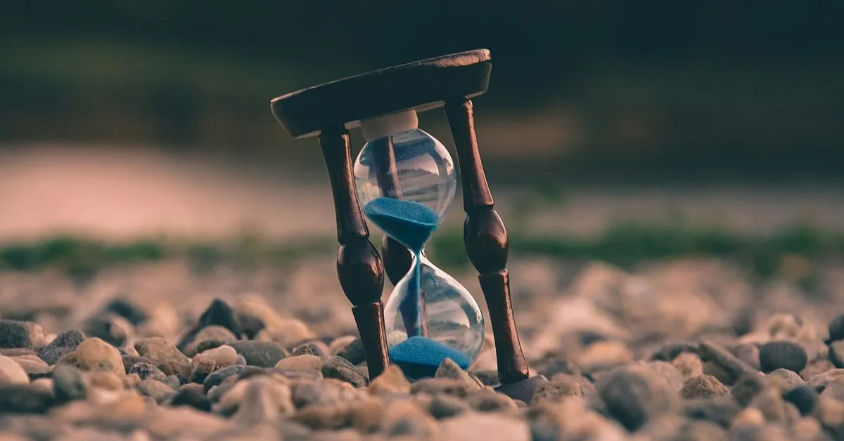 Tilted hourglass on pebbles representing the moment every startup needs security leadership, from IOmergent fractional CISO services.