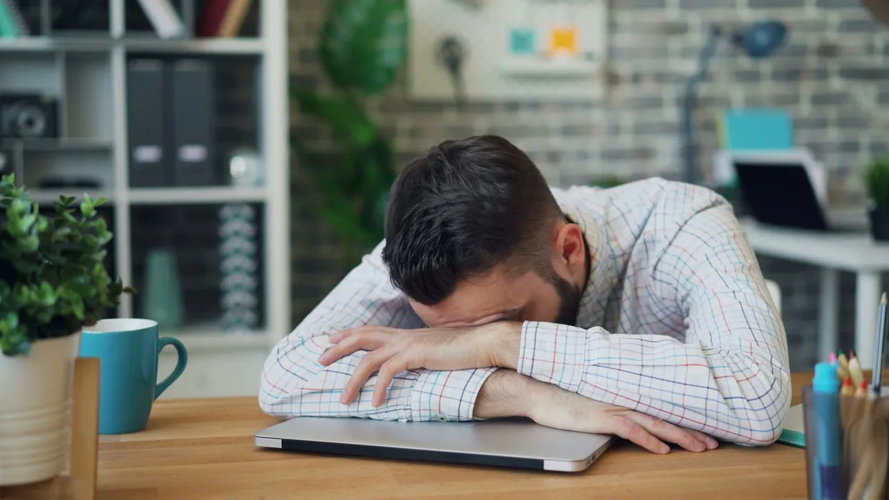 Exhausted security professional with head down on laptop, overwhelmed by cloud security alerts that IOmergent managed CSPM helps prioritize.